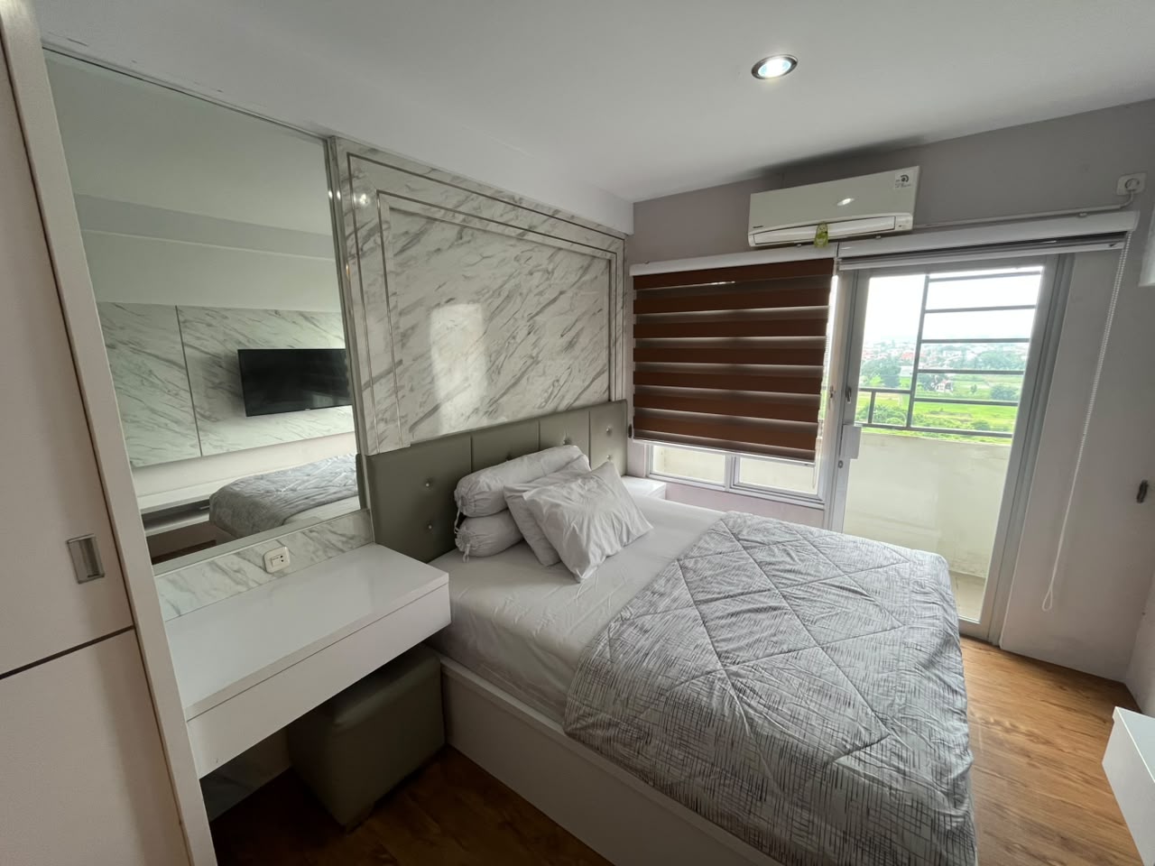 Area tidur studio dengan headboard marmer dan cermin